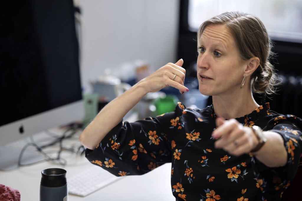 Zijaanzicht van Felienne die met één hand gebaart alsof ze aan het bellen is en met de andere naar voren wijst. 