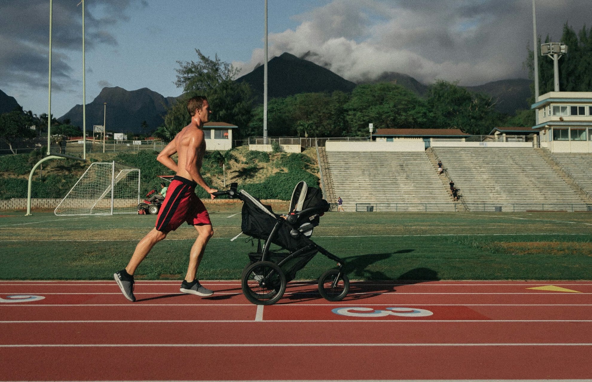 Een man jogt over een atlethiekbaan met een kinderwagen.